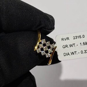 May include: A gold ring with a diamond-studded square design. The ring features a series of small, clear diamonds set in a grid pattern. The ring is held against a black background, with a tag visible that includes the text "RVR 2315.0".