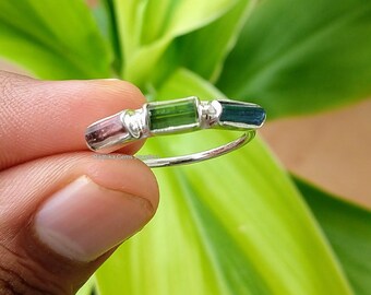 May include: A silver ring with three rectangular gemstones. The gemstones are pink, green, and blue. The ring is on a finger.