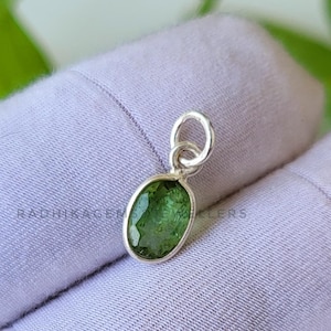 Könnte beinhalten: Ein silberner Anhänger mit einem grünen ovalen Edelstein. Der Anhänger befindet sich auf einem weißen Hintergrund.