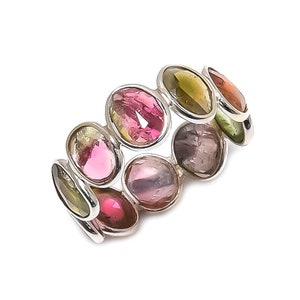 Puede incluir: Un anillo de plata con una banda de piedras preciosas ovaladas en tonos de rosa, verde y morado.