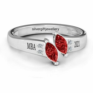May include: Silver ring featuring two red marquise-shaped stones and two small clear stones. The ring is engraved with "MBA" and "2021".