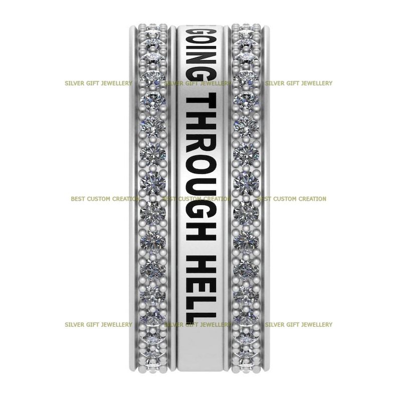 Op de afbeelding: Een zilveren ring met een band van kleine heldere stenen en de woorden "GOING THROUGH HELL" gegraveerd aan de zijkant.