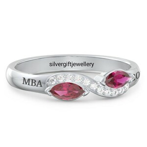 May include: A silver ring with two marquise-shaped red gemstones and a row of clear cubic zirconia stones. The ring is engraved with the letters "MBA".