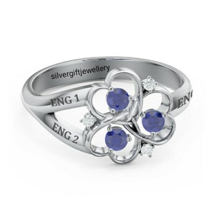 May include: A silver ring with three blue gemstones set in a heart-shaped design. The ring is engraved with the words "ENG 1" and "ENG 2".