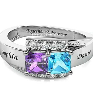 May include: A silver ring with two square-shaped gemstones, one purple and one blue, set in a silver band with a row of smaller clear gemstones. The ring is engraved with the words "Sophia" and "Danie" and the phrase "Together & Forever".