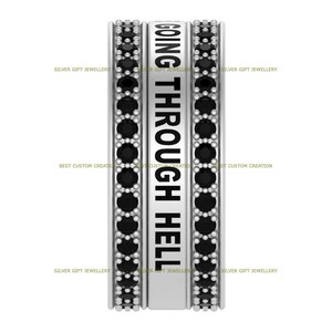 Op de afbeelding: Een zilveren ring met zwarte stenen rond de band. De ring heeft de woorden "GOING THROUGH HELL" gegraveerd.