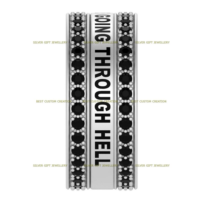 Op de afbeelding: Een zilveren ring met zwarte stenen rond de band. De ring heeft de woorden "GOING THROUGH HELL" gegraveerd.