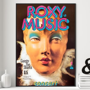 May include: A vintage Roxy Music concert poster. The poster features a stylized face with blue eyeshadow and pink lips. The band's name is in large, bubble-style letters with a blue and pink colour scheme. The poster includes the text "Guests: The Sharks 8.5."