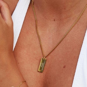 May include: A gold chain necklace with a rectangular pendant and a gold chain bracelet with a round pendant that says "LYF".