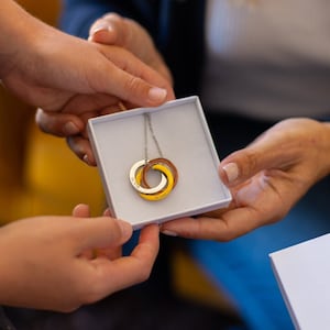 May include: A white box with a gold, silver, and copper interlocking ring necklace inside. The box has the words "CUSTOMCUFF" printed on it.