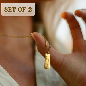 May include: A gold chain necklace with a small rectangular pendant engraved with coordinates. The pendant is being held by a hand. The text on the pendant reads "48.8512 76N 2.2916 48E". The image is labeled "SET OF 2".