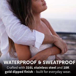May include: A couple embracing, with the woman's arm around the man's neck. The text "WATERPROOF & SWEATPROOF" is at the bottom of the image. The text "Crafted with 316L stainless steel and 18K gold dipped finish - built for everyday wear." is below the first line of text.
