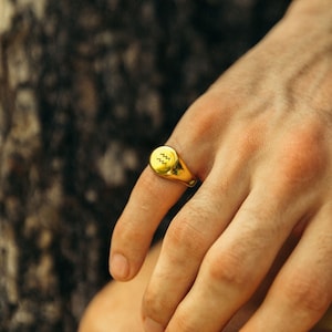 May include: A gold signet ring with the Aquarius zodiac symbol engraved on the top.