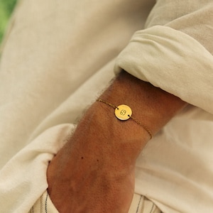 May include: A gold chain bracelet with a round gold charm that has the number "69" engraved on it.