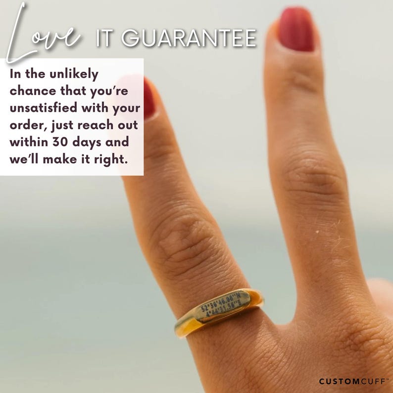 Puede incluir: Un anillo de oro con una inscripci&oacute;n personalizada que dice "52 36 46.08 N 4.91 13.91 E". El anillo est&aacute; en un dedo, y el fondo es una imagen borrosa de una playa.