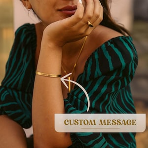 May include: A gold bracelet with the inscription "Everything happens for a reason" on a person's wrist. The bracelet is shown against a green and black striped background.  CUSTOM MESSAGE