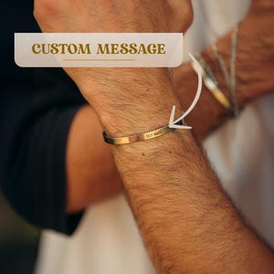 May include: A gold metal bracelet with the words "SELF MADE" engraved on it.