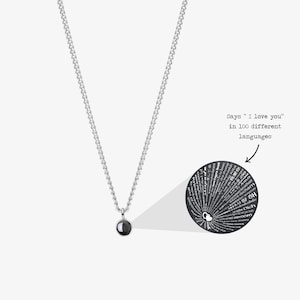 May include: A silver chain necklace with a black round pendant. The pendant has the words "I love you" inscribed in 100 different languages.