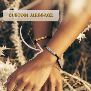 May include: Two black cord bracelets with silver and gold metal plates. The plates have engraved text that reads "FOREVER YOUNG" and "TWENTY FIRST BIRTHDAY".