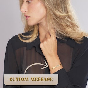 May include: A gold chain bracelet with a rectangular nameplate that can be personalized with a custom message. The bracelet is shown on a model's wrist.