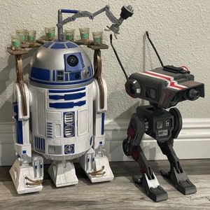 Puede incluir: Un juguete robot R2-D2 blanco y gris con un portavasos y un juguete robot droide negro y gris con detalles rojos.