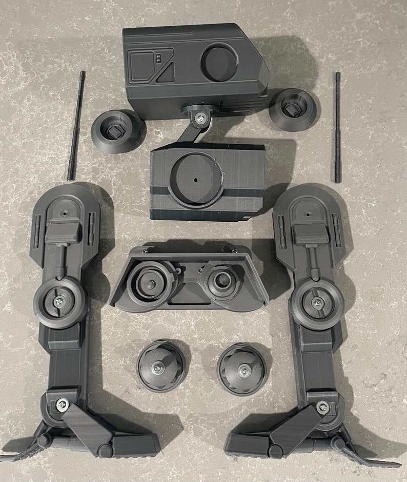 Puede incluir: Un modelo de robot impreso en 3D negro desmontado con m&uacute;ltiples partes, incluyendo una cabeza, piernas y ruedas.