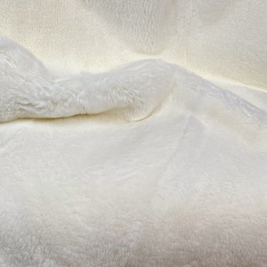 May include: A white faux fur throw blanket with a soft, fluffy texture.