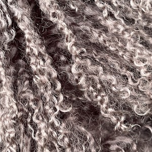 May include: Close-up of a dark brown curly fur texture. The fur is soft and fluffy, with a slightly grey undertone.