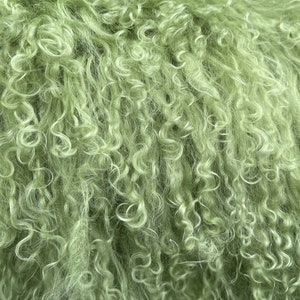 Puede incluir: Primer plano de una tela de piel suave, rizada y de color verde. La piel es muy densa y tiene una textura esponjosa.