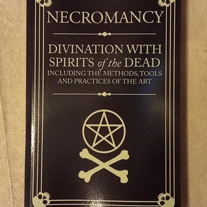 May include: A dark book titled "NECROMANCY" with the subtitle "DIVINATION WITH SPIRITS of the DEAD." The cover features a pentagram, crossed bones, and skull illustrations. The book's design includes a border with skull motifs.