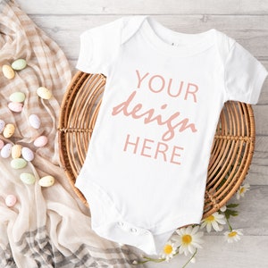 May include: White baby onesie with short sleeves on a wicker basket with the text "YOUR design HERE" in pink.