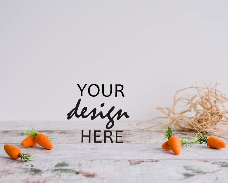 May include: A whitewashed wooden surface with the text "YOUR design HERE" in black.  There are five orange carrots with green stems scattered on the surface.  A pile of straw is in the background.