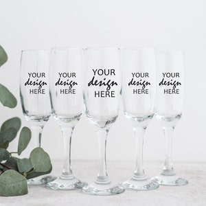 May include: Five clear glass champagne flutes with black text that reads "YOUR design HERE" on each flute.