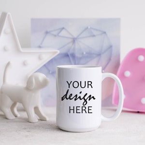 May include: White ceramic mug with a black inscription that reads "YOUR design HERE". The mug is sitting on a white surface with a white star, a white dog figurine, and a pink heart-shaped light in the background.
