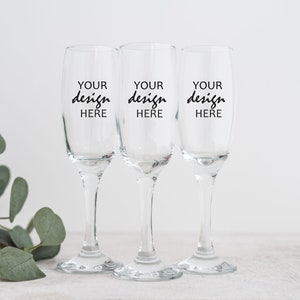 May include: Three clear glass champagne flutes with black text that reads "YOUR design HERE" on each flute.