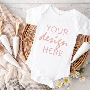 May include: White baby onesie with short sleeves and a popper fastening. The onesie has the text "YOUR design HERE" printed in pink on the front.
