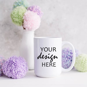 May include: White ceramic mug with the text "YOUR design HERE" in black lettering. The mug is surrounded by colorful pom-poms.