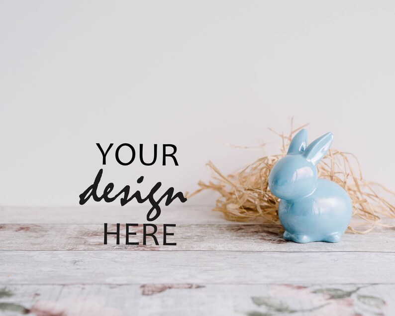 May include: A light blue ceramic bunny figurine sitting in a nest of straw on a whitewashed wooden surface. The text "YOUR design HERE" is written in black on the white background.