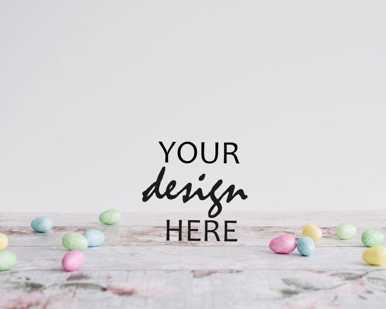 May include: A white background with the text "YOUR design HERE" in black cursive writing.  A light wood surface with pastel colored Easter eggs scattered across it.