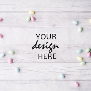 May include: A white wooden background with pastel colored candy eggs scattered around the edges. The text "YOUR design HERE" is in the center of the image.