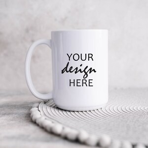 May include: White ceramic mug with a black inscription that reads "YOUR design HERE" on a white circular coaster.