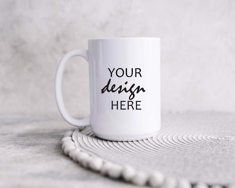 May include: White ceramic mug with a black inscription that reads "YOUR design HERE" on a white circular coaster.