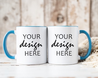 Puede incluir: Dos tazas de cerámica blanca con bordes y asas azules. Las tazas tienen el texto "YOUR design HERE" impreso en ellas.