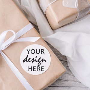 May include: A brown paper gift box with a white ribbon and bow. A white circle sticker with the text "YOUR design HERE" is on the box.