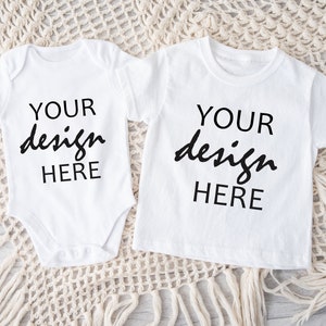 Puede incluir: Dos camisetas blancas para bebé, una un body y otra una camiseta, con el texto "YOUR design HERE" impreso en cada una.