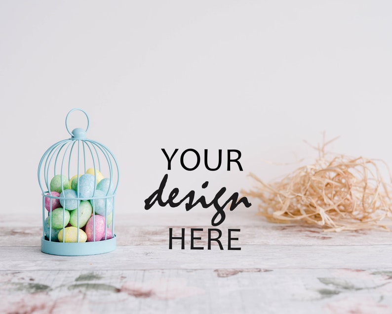May include: A light blue birdcage filled with pastel colored Easter eggs. The cage is sitting on a whitewashed wooden surface with the text "YOUR design HERE" written in black.