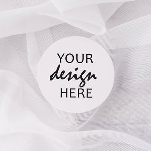 May include: White round coaster with black text that says "YOUR design HERE" on a white sheer fabric background.