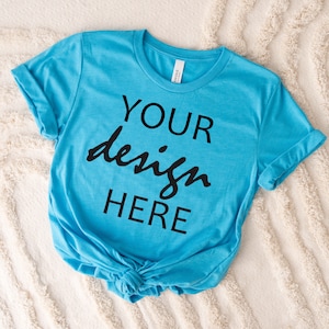 May include: A turquoise blue t-shirt with the text "YOUR design HERE" printed in black on the front.