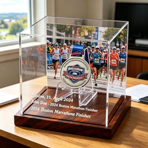 Könnte beinhalten: Eine transparente Acryl-Vitrine mit Holzsockel, die eine Medaille eines Boston Marathon-Finisher präsentiert. Die Medaille ist silberfarben mit einem blauen Band. Das Gehäuse enthält ein Foto von Läufern und den Text: "Boston, 15. April 2024 John Doe - 2024 Boston Marathon Finisher 2024 Boston Marrathone Finisher."