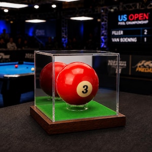May include: A bright red billiard ball with the number 3 printed in black on a cream-colored circle. The ball is displayed inside a clear acrylic cube case with a green felt base and a dark wooden bottom, resting on a black surface.